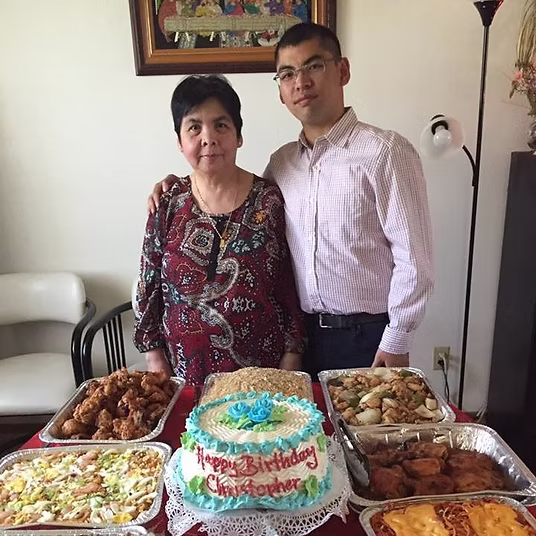 Chris stands with his mother in front of a beautiful spread of Filipino food and a cake that reads, Happy Birthday Christopher.